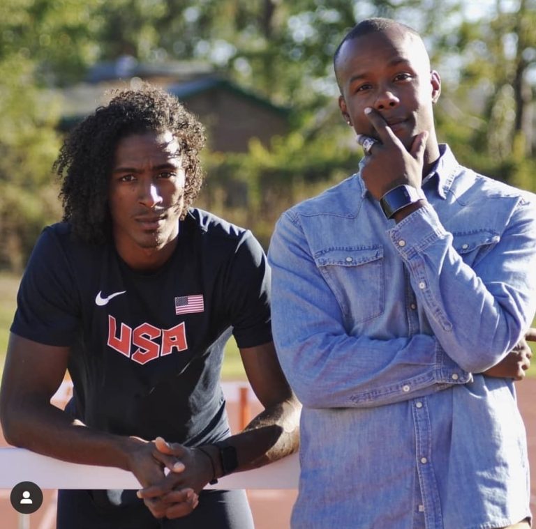 Coach Lawrence Superstar Terry standing beside U.S. hurdler Jarret Eaton at a track.